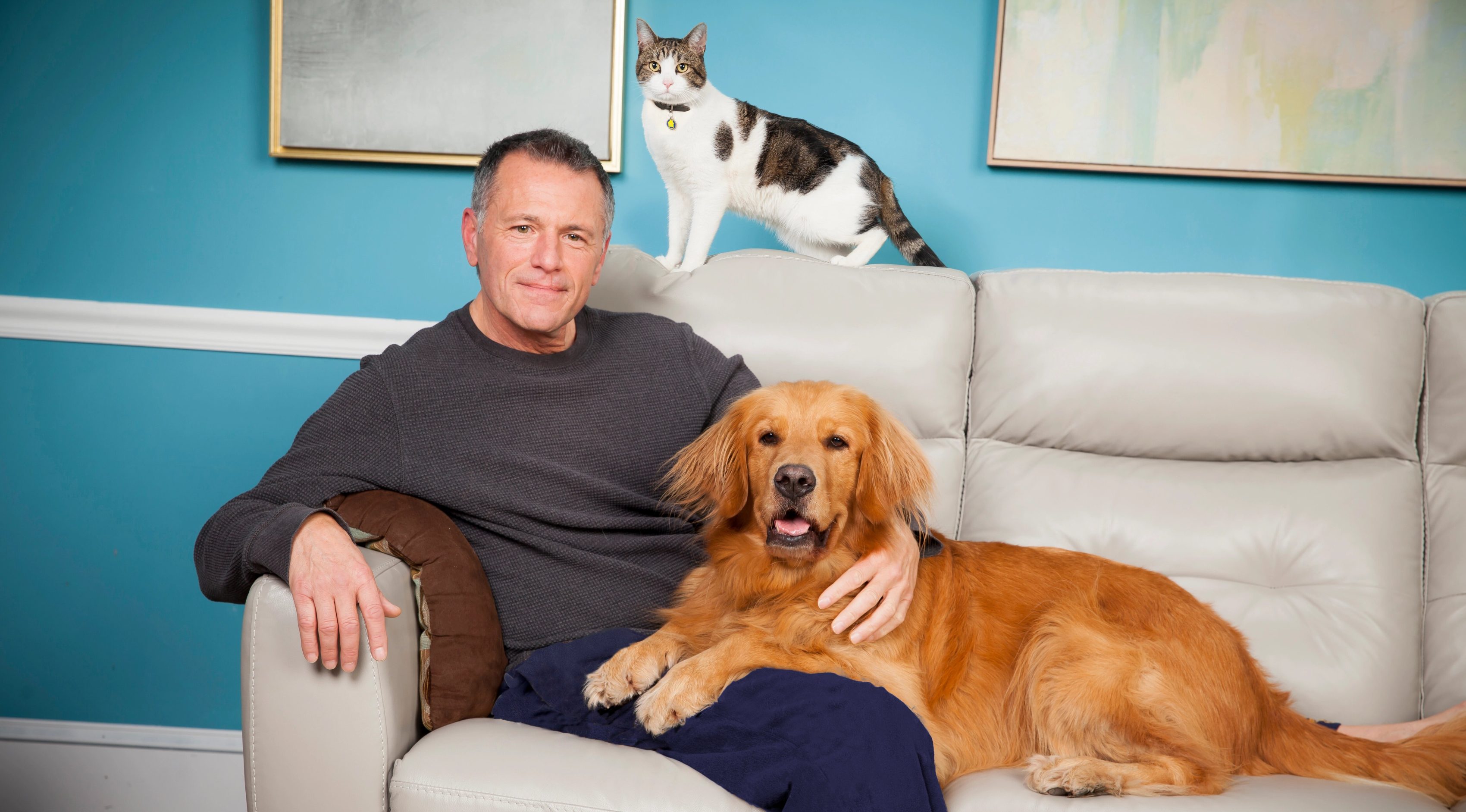 Male pet owner sitting on couch with his golden retriever and cat.
