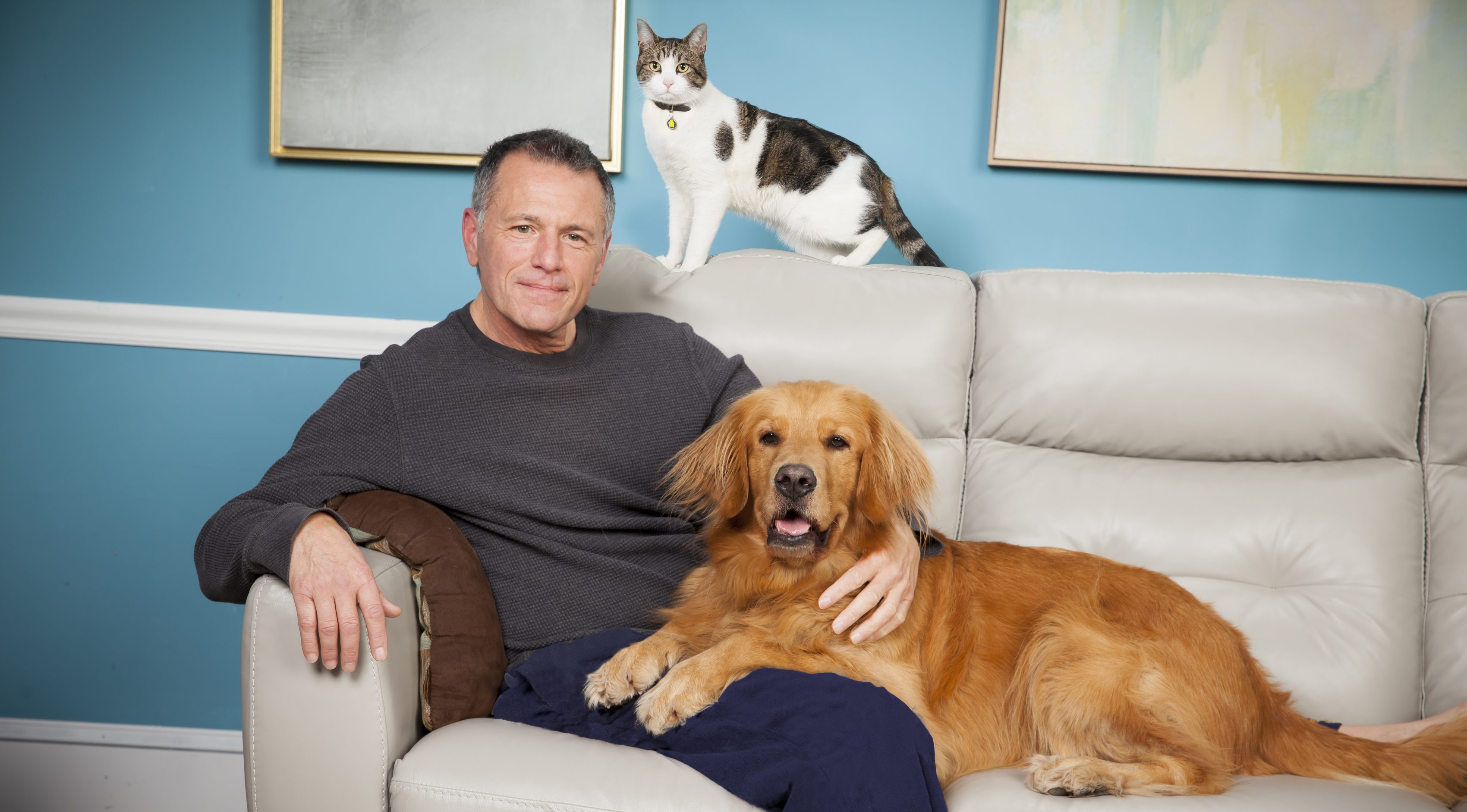 Male pet owner sitting on couch with his golden retriever and cat.